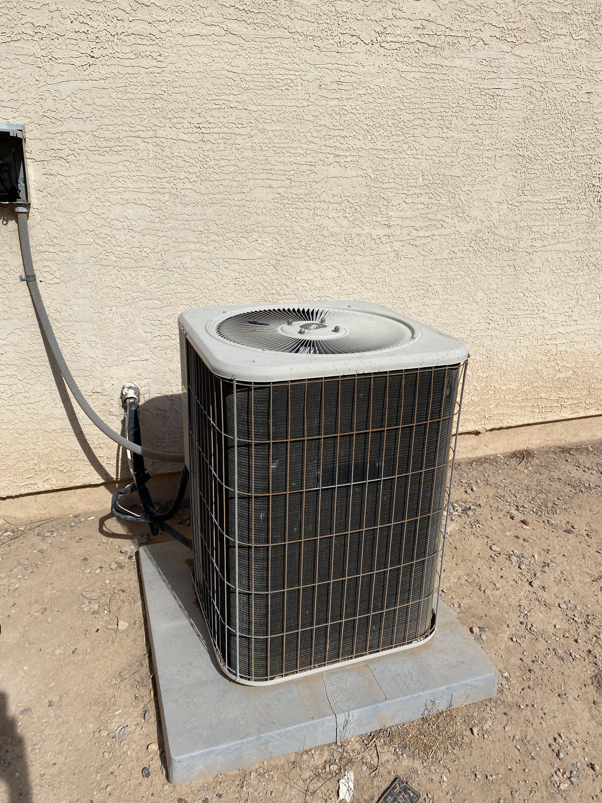 An older residential split system condenser on its pad beside a stucco wall