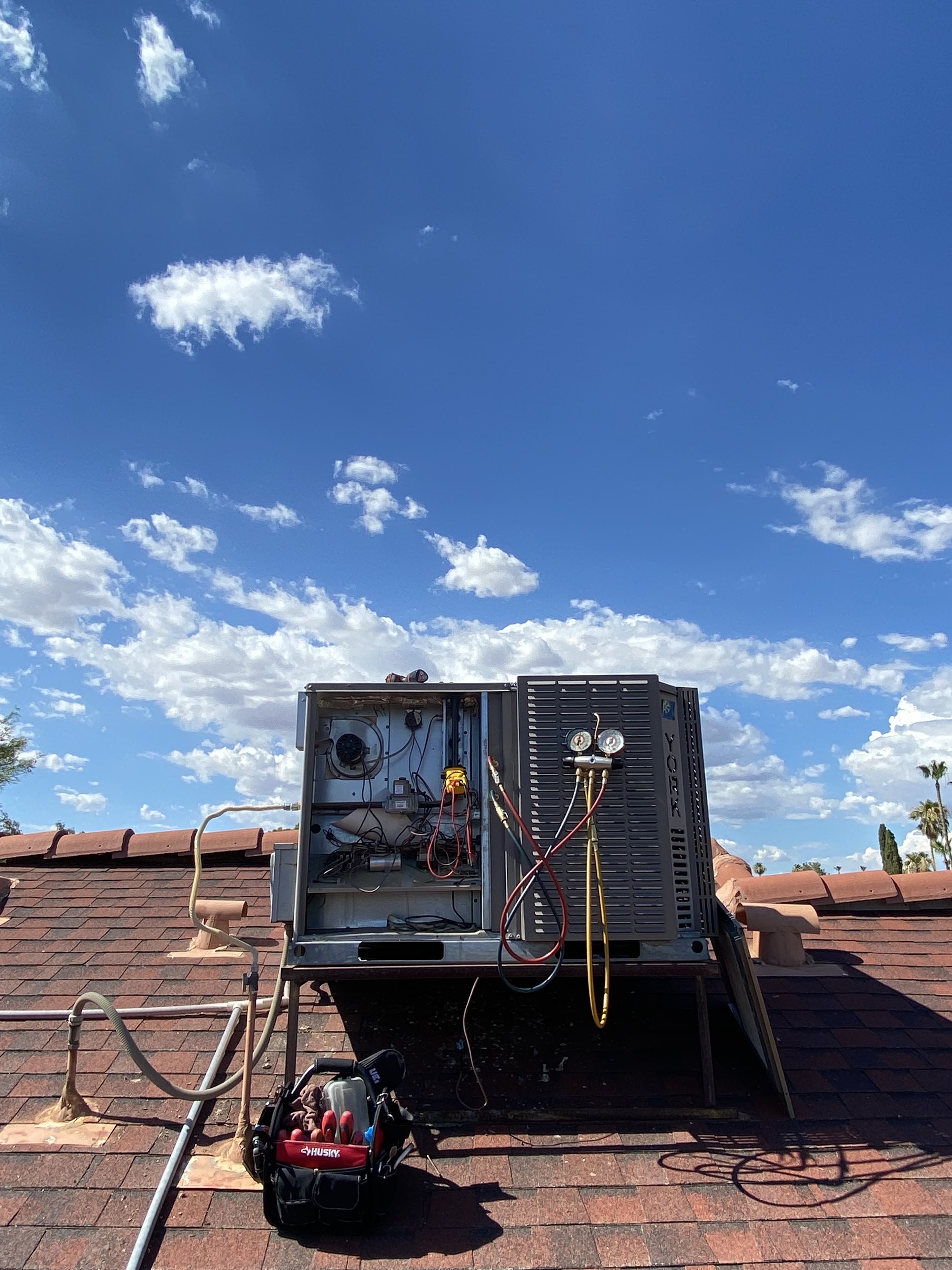 A York package unit open on a tile roof with manifold gauges connected and a tool bag alongside