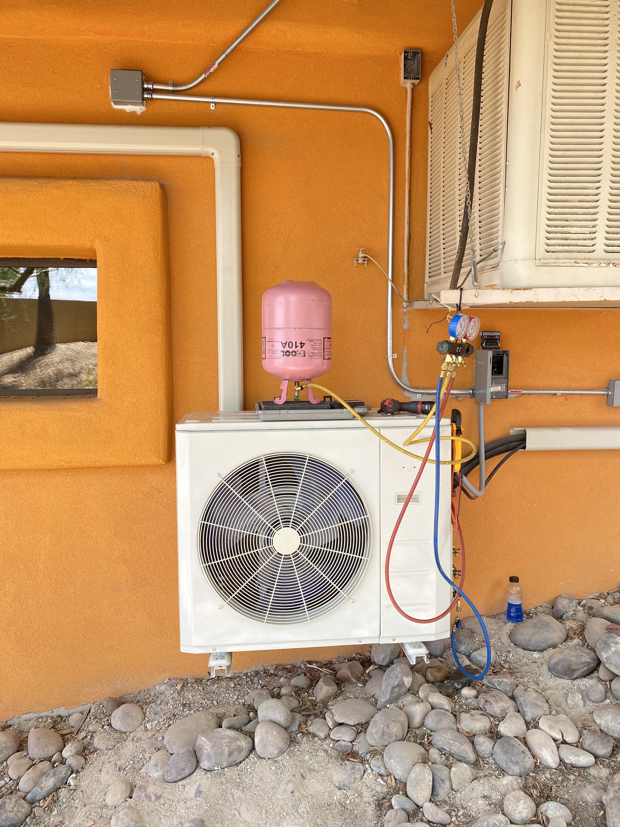 A newly installed ductless mini split condenser being charged against an orange stucco wall