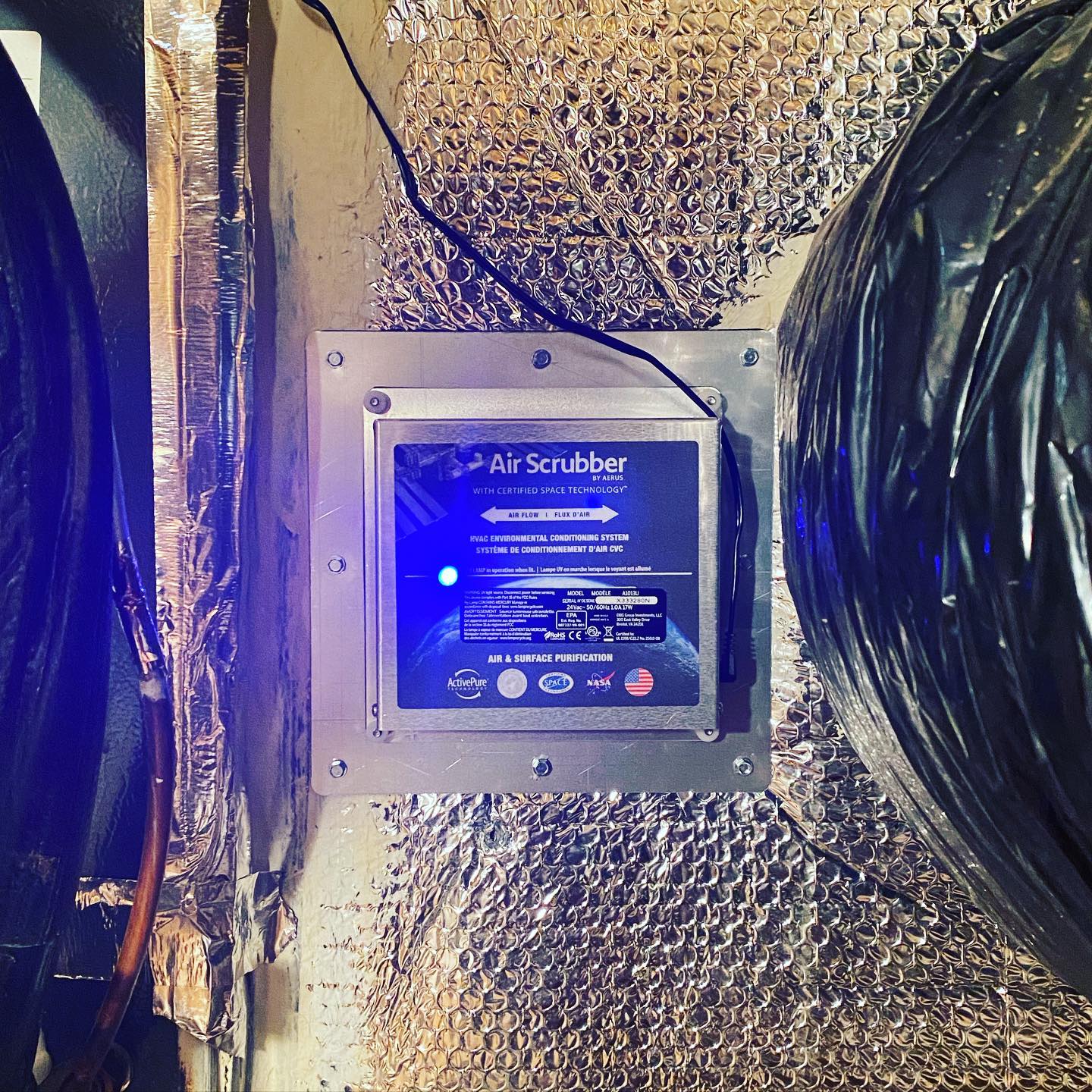 An Air Scrubber by Aerus installed into insulated ductwork with its lamp lit